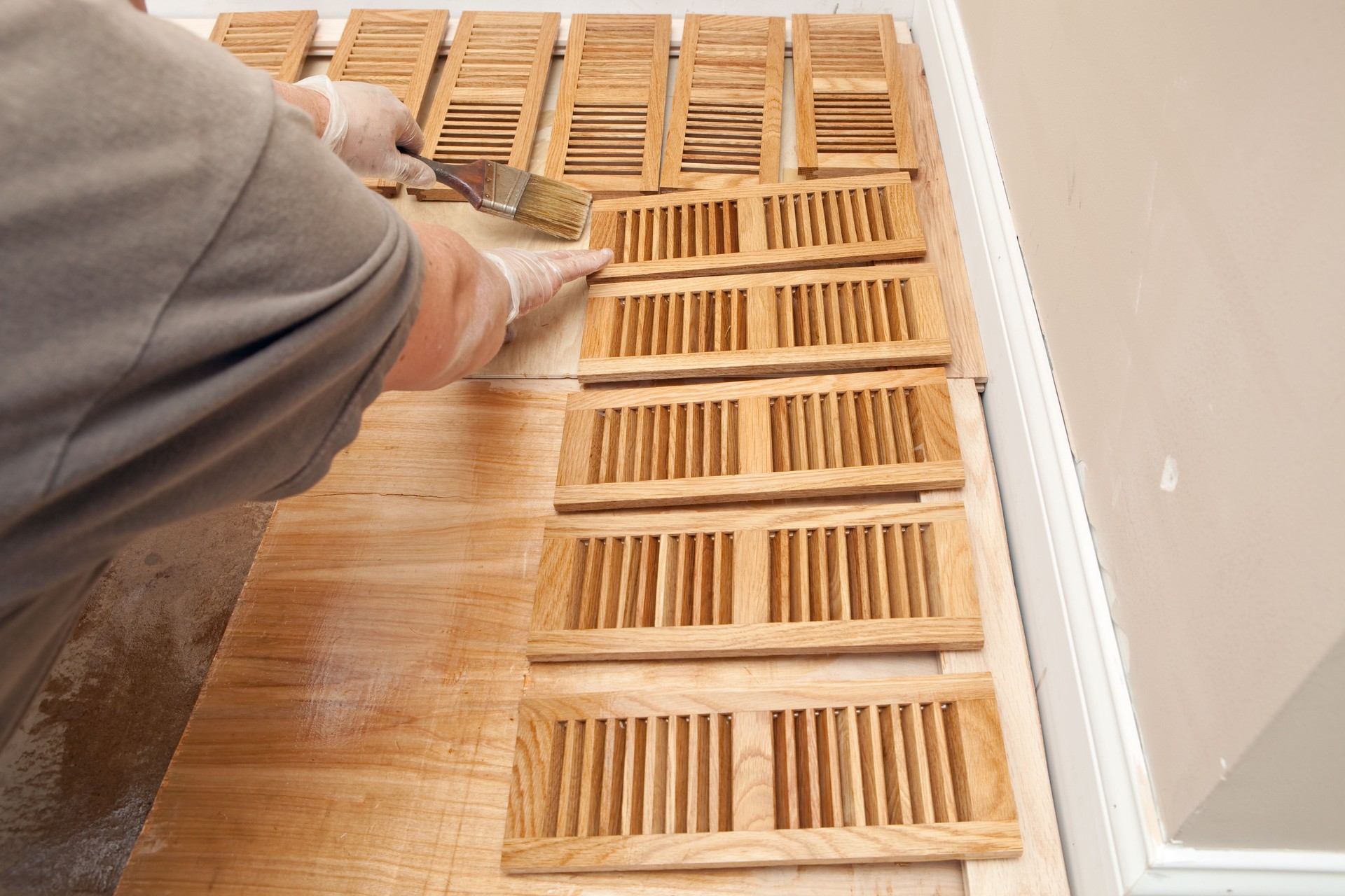 Painter Brushing Clear Polyurethane on Hardwood Floor Vent Grates